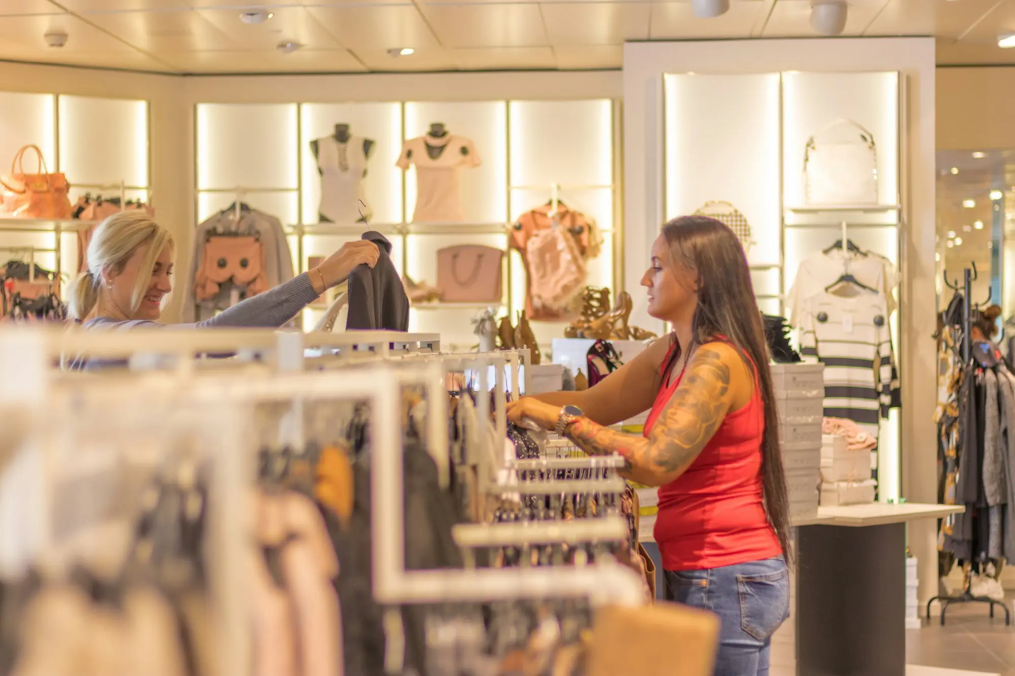 Two people sorting garments on racks inside a bright retail shop